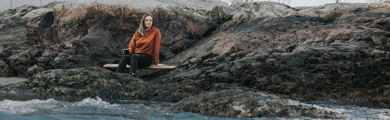 Girl on Rocks by the ocean in Orange Hoodie