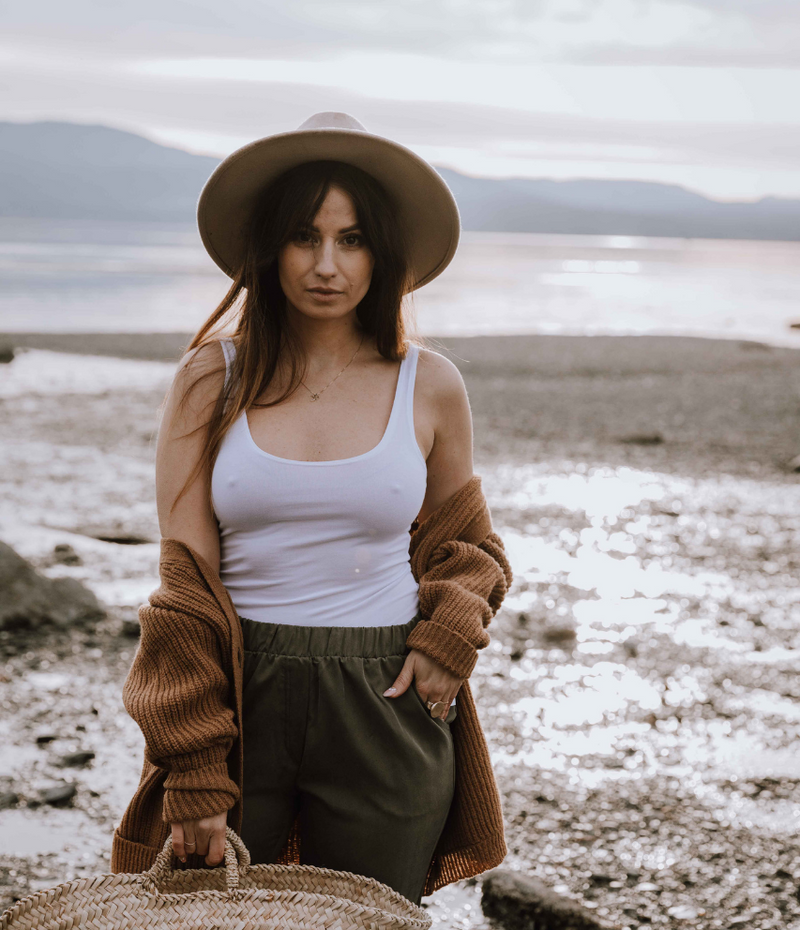 Woman on beach wearing white tank top and wide-brim hat